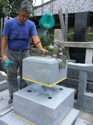 墓石を設置する工事。小さなクレーンを使用して慎重に行う